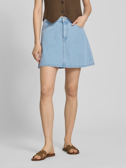 Vrouwenmodel draagt A-lijn jeansrok uit katoenmix met viscose, denimlook in lichtblauw, 5-pocketmodel, Pieces model 'ABBI', minilengte, knoop- en ritssluiting, materiaalverwerking twill, detailopname onderlichaam, voorkant.