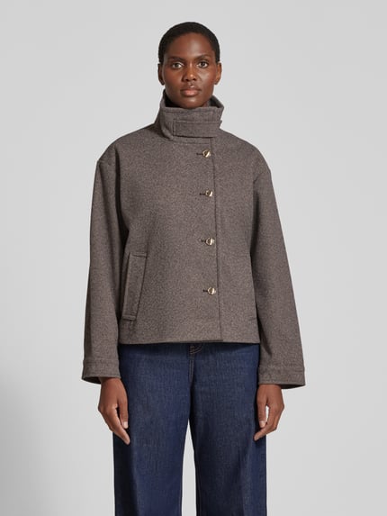 Frauenmodel trägt Bomberjacke mit hohem Stehkragen von VERO MODA in Braun-Grau, weiche Textur, kombiniert mit blauen Jeans, Ganzkörperansicht von vorne. Damen Teddy- / Webpelzjacke.