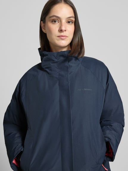Frauenmodel trägt Parka mit echter Daune und 10.000 mm Wassersäule von Peak Performance in Dunkelblau, Nahaufnahme Oberkörper. Damen Parka Regular Fit, Modell TREELINE, Kapuze, verdeckter Reißverschluss, Rückenlänge 108 cm, Schulterbreite 53 cm, Brustweite 62 cm, Ärmellänge 49 cm.