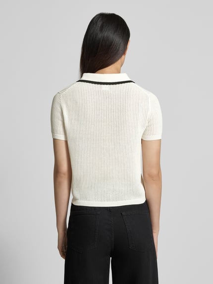 Modelka kobieca nosi Regular Fit Strick-Shirt aus reiner Baumwolle Modell 'SLYSA' od HUGO, kolor jednolity, faktura strukturalna, logo, kontrastowy pasek, krótkie rękawy z ściągaczem, dzianina, widok całej sylwetki od tyłu.