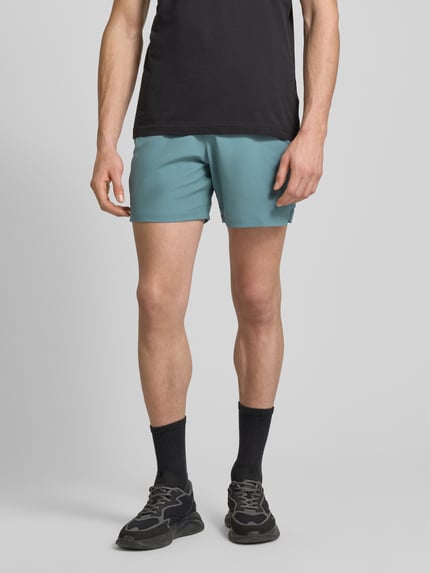 Mężczyzna nosi Szorty z elastycznym pasem i logo od Under Armour, krój regular fit, label-detal, kolor niebieskozielony, zdjęcie: całe nogi widoczne z przodu. Szerokość w pasie M: 39 cm, długość wewnętrzna nogawki: 17 cm.