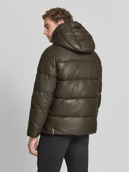 Männermodel trägt kurtka pikowana z kapturem Modell 'COEN 2' von khujo, krój regular fit, detal z zamkiem błyskawicznym, detal z logo, kolor oliwkowy, gładka faktura, Długość tyłu w rozmiarze M: 72 cm, szerokość ramion w rozmiarze M: 55 cm, szerokość klatki piersiowej w rozmiarze M: 61 cm, długość rękawów w rozmiarze M: 62 cm, Ganzkörperansicht Rückansicht.
