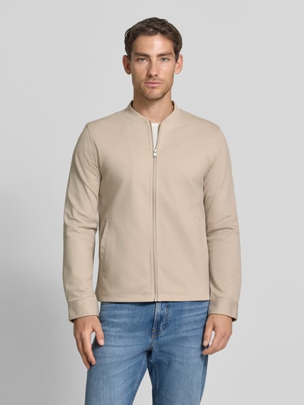 Männermodel trägt Slim Fit Sweatjacke mit Stehkragen von Lindbergh, Mieszanka materiałów z dodatkiem streczu, zamek błyskawiczny, wpuszczane kieszenie, Długość tyłu w rozmiarze M: 67 cm, Długość rękawów w rozmiarze M: 66 cm, jasnobeżowy, krój slim fit, Ganzkörperansicht von vorne.