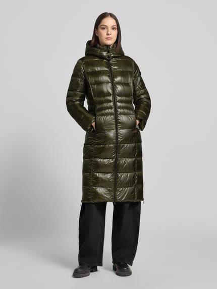Frauenmodel trägt glänzenden, olivgrünen Puffer Coat mit Kapuze Modell 'DALIA LONG' von FRIEDA & FREDDIES, unifarben, Longline, Logo-Patch, Zweiwege-Reißverschluss, Reißverschlusstaschen, Taft-Material, Ganzkörperansicht von vorne.