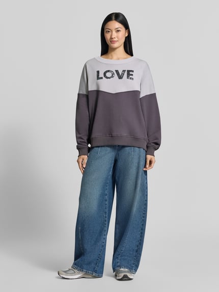 Frauenmodel trägt Oversized Sweatshirt aus reiner Baumwolle von miss goodlife in Grau mit Paillettenbesatz, gerippten Abschlüssen, Ganzkörperansicht von vorne.