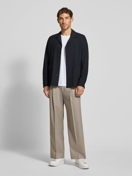 Männermodel trägt Oversized Fit Freizeithemd mit Viskose-Anteil Modell 'Malte' von CINQUE, dunkelblau, beige Hose, weiße Schuhe, Ganzkörperansicht von vorne. Elastischer Material-Mix, Reverskragen, langärmelig, Rückenlänge 75 cm bei Größe M.