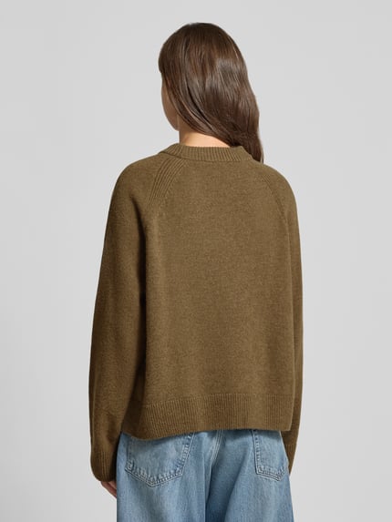 Frauenmodel trägt Loose Fit Pullover aus reiner Wolle von ARMEDANGELS in Olivgrün, strukturierte Strickoptik, Ganzkörperansicht Rückansicht.