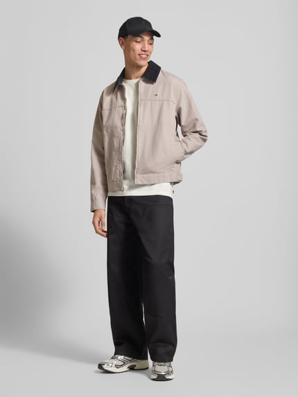 Männermodel trägt Regular Fit Ranch-Jacke aus reiner Baumwolle von Tommy Jeans in Beige, Umlegekragen aus Cord, Ganzkörperansicht von vorne.
