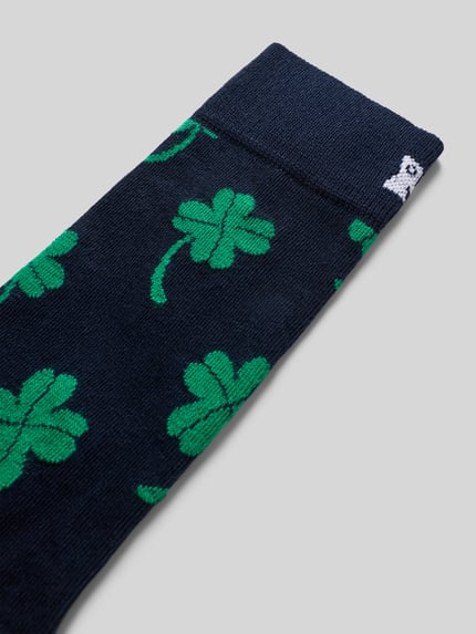 Produktfoto, Socken mit Allover-Motiv-Print von Happy Socks, dunkelblauer Baumwoll-Mix mit grünen Kleeblättern, Label-Detail sichtbar.