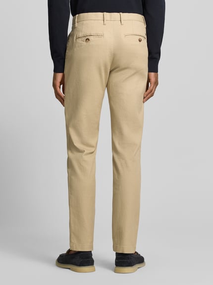 Männermodel trägt Slim Fit Chino aus bawełny-mix von Tommy Hilfiger, jednokolorowy, wyhaftowane logo, kieszenie z guzikami, pika, Ganzkörperansicht Rückansicht.
