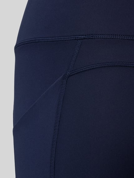 Frauenmodel trägt Flared Fit Leggins mit breitem Bund Modell 'OASIS' von Fabletics, dunkelblauer Elastikstoff, Detailaufnahme.