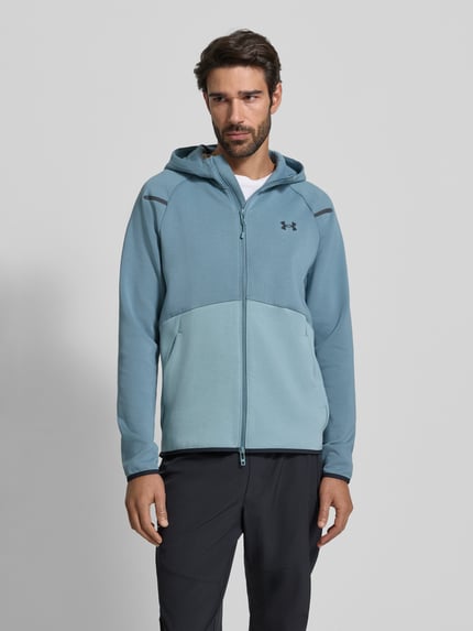 Męski model nosi Kurtka treningowa z zamkiem błyskawicznym dwustronnym model 'Unstoppable' od Under Armour, mieszanka bawełny, krój regular fit, kaptur, długość tyłu 71 cm, długość rękawów 60 cm, widok całej sylwetki z przodu.