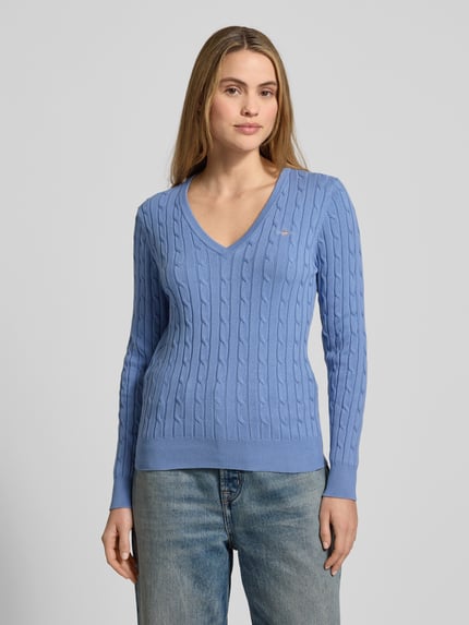 Frauenmodel trägt Strickpullover mit Zopfmuster und Label-Stitching von Gant, Baumwoll-Mix mit Stretch-Anteil, Slim Fit, V-Ausschnitt, hellblau mit feiner Strickstruktur, Damenmodell, Ganzkörperansicht von vorne.