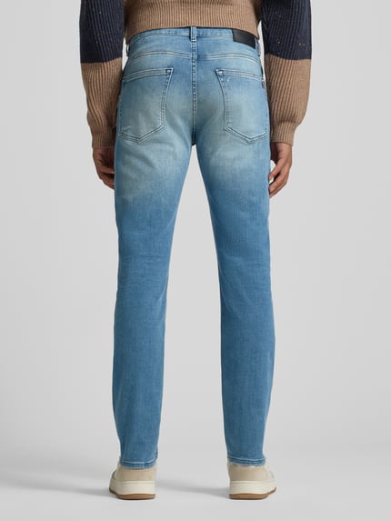 Męski model nosi Slim Fit Jeans aus Baumwoll-Mix Modell 'DELAWARE' von BOSS Orange, stylizowana na denim, 5 kieszeni, jasnoniebieski, naszywka z logo, szlufki, mieszanka bawełny, fason slim straight fit, zapięcie na guzik i zamek, Ganzkörperansicht Rückansicht.