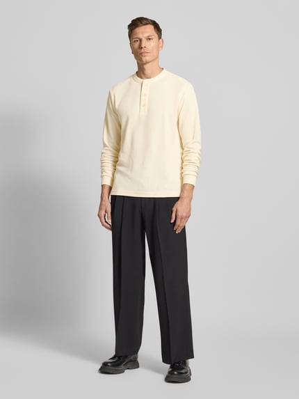 Männermodel trägt Regular Fit Pullover mit Knopfleiste Modell 'Kilano' von Drykorn im Baumwoll-Mix, cremefarben, Ganzkörperansicht von vorne.