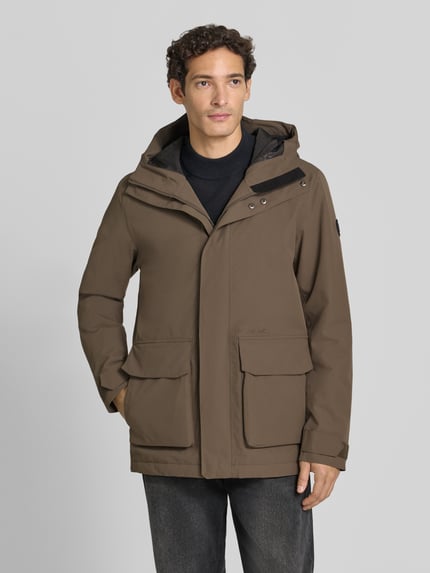 Männermodel trägt Regular Fit Jacke mit aufgesetzten Taschen Modell 'Liam' von Didriksons in Braun mit Kapuze, Ganzkörperansicht von vorne. Rückenlänge 79 cm, Schulterbreite 44 cm, Brustweite 45 cm, Ärmellänge 70 cm.