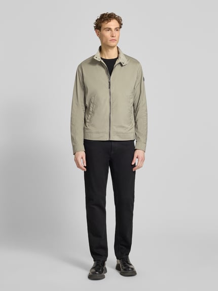 Männermodel trägt Jacke mit Stehkragen Modell 'Vicente' von JOOP! Collection in Regular-Fit, Reißverschluss, Eingrifftaschen, beige, Ganzkörperansicht von vorne. Rückenlänge 66 cm, Schulterbreite 46 cm, Brustweite 52 cm, Ärmellänge 67 cm.