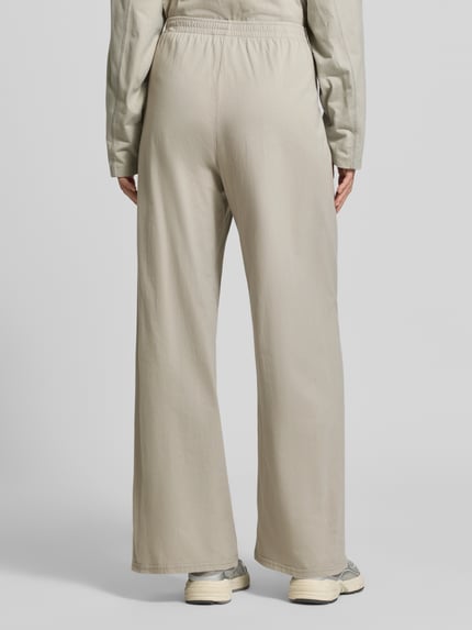 Frauenmodel trägt Wide Fit Hose aus reiner Baumwolle Modell 'GIXY' von American Vintage in Beige, elastischer Bund, Ganzkörperansicht Rückansicht.