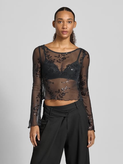 Frauenmodel trägt Langarmshirt mit ausgestelltem Ärmelabschluss von PIECES, schwarzes Mesh mit floralem Allover-Spitzenmuster, U-Boot-Ausschnitt, Nahaufnahme Oberkörper.