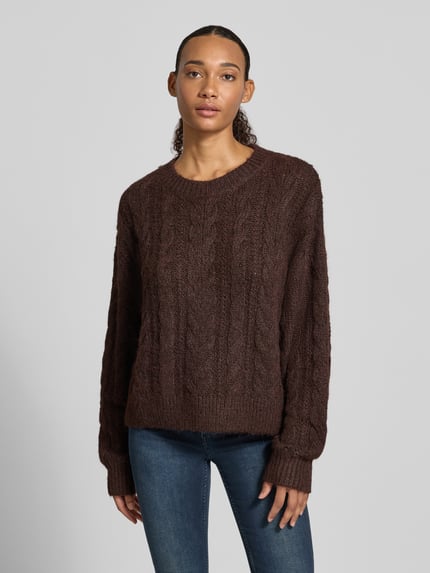 Frauenmodel trägt Oversized Fit Strickpullover mit Zopfmuster von REVIEW in Dunkelbraun, Rundhalsausschnitt, elastische Abschlüsse, Rückenlänge 54 cm, Ärmellänge 58 cm, Ganzkörperansicht von vorne.