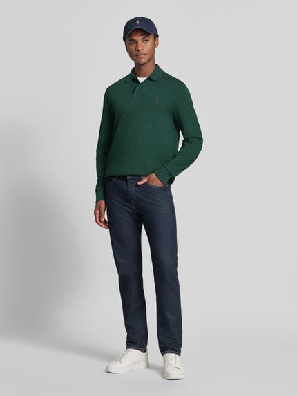 Männermodel trägt Regular Fit Poloshirt aus reiner Baumwolle von Polo Ralph Lauren in Dunkelgrün, kombiniert mit Jeans, Ganzkörperansicht von vorne, Herren Poloshirt von Polo Ralph Lauren.