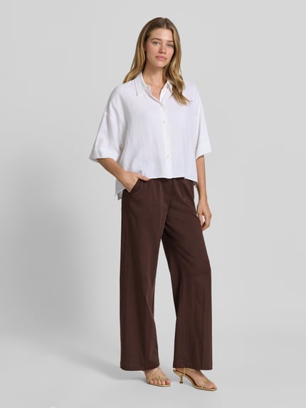 Kobiece model prezentuje spodnie materiałowe z mieszanki bawełny z dodatkiem streczu OPUS PANTS, krój loose fit, model 'Mucia Base', kolor brązowy, z wpuszczanymi kieszeniami francuskimi i tylnymi kieszeniami z wypustką, elastyczny pas, szerokość w rozmiarze 36: 31 cm, długość wewnętrzna nogawki: 80 cm, widok całej sylwetki z przodu.
