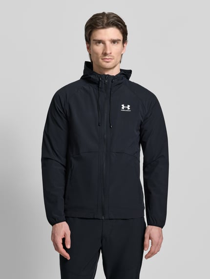 Männermodel trägt schwarze Jacke mit Kapuze von Under Armour mit Label-Print, Reißverschluss, lockerer Schnitt, Ganzkörperansicht von vorne.