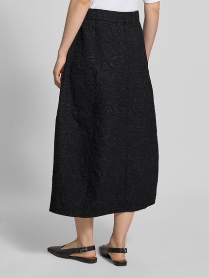 Männermodel trägt Midirock im Allover-Look Modell 'ROSIE' von Copenhagen Muse, czarny kolor, fakturowany materiał, elastyczny pas, A-linia, Szerokość w rozmiarze S: 37 cm, długość całkowita: 82 cm, Ganzkörperansicht Rückansicht