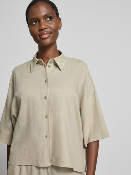Vrouwenmodel draagt Relaxed Fit Bluse aus Leinen-Viskose-Mix van Drykorn, lichtbeige, kentkraag, knoopsluiting, dames blouse, mix van linnen en viscose, model 'YARIKA', ruglengte maat 36 55 cm, mouwlengte 23 cm, overgeslagen schouders, detailopname bovenlichaam.