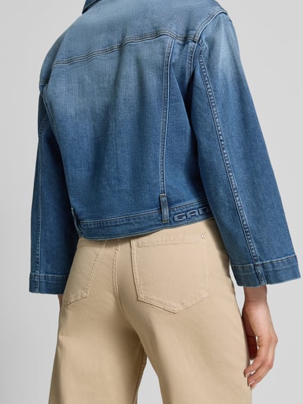 Männermodel trägt Jeansjacke im Used-Look mit Label-Detail Modell 'Tina' od Gang, bawełna z elastanem, krój relaxed fit, detal z logo, długość tyłu w rozmiarze S 54 cm, szerokość ramion w rozmiarze S 49 cm, szerokość w biuście w rozmiarze S 46 cm, długość rękawa w rozmiarze S 54 cm, beżowe spodnie, widok całej sylwetki z tyłu
