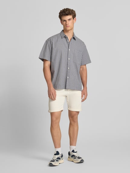 Männermodel trägt Jeansshorts mit Umschlag und Eingrifftaschen Modell 'RICK ALLEN' von Jack & Jones aus Baumwoll-Elasthan-Mix, Regular-Fit, Farbton hell, Struktur glatt, Bundweite 43 cm, Innenbeinlänge 20 cm, Ganzkörperansicht von vorne.