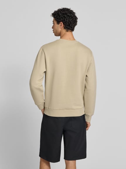 Mannelijk model draagt Sweatshirt mit Rundhalsausschnitt und Label-Stitching van Carhartt Work In Progress in beige, mix van katoen en elastaan, regular fit, ronde hals, labelstitching, ruglengte maat M 68 cm, mouwlengte maat M 65 cm. Ganzkörperansicht Rückansicht.