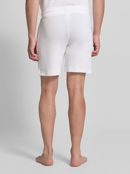 Männermodel trägt Regular Fit Sweatshorts aus Baumwoll-Mix Modell 'AUSTIN' von HUGO in Weiß, strukturierte Oberfläche, Herren Sweatshorts, Ganzkörperansicht Rückansicht.