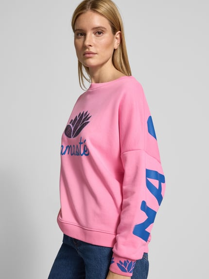 Frauenmodel trägt Oversized Sweatshirt mit gerippten Abschlüssen von miss goodlife in Rosa mit blauen Aufdrucken, Ganzkörperansicht von vorne.