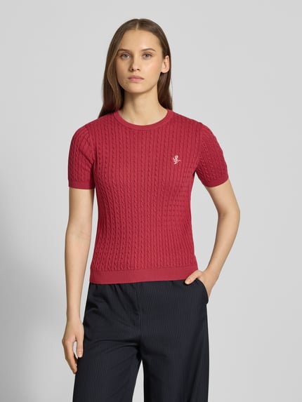 Frauenmodel trägt Kurzarmpullover mit Zopfmuster und Rundhalsausschnitt von Review aus reiner Baumwolle, Slim-Fit, Logo, Rippbündchen; Nahaufnahme Oberkörper.