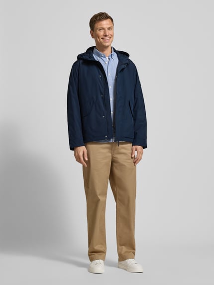 Männermodel trägt Regular Fit Funktionsjacke mit Kapuze von Tommy Hilfiger, Optik: Unifarben, wasserabweisend, Ganzkörperansicht von vorne.