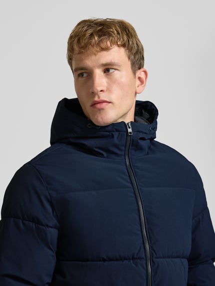 Männermodel trägt Steppjacke mit Kapuze Modell 'GALAXY' von JACK & JONES in Dunkelblau, strukturierte Oberfläche, Nahaufnahme Oberkörper. Kontext: Herren Steppjacke Regular Fit, Reißverschluss, Eingrifftaschen, Kapuze mit Tunnelzug, Rückenlänge 70 cm, Schulterbreite 49 cm, Brustweite 58 cm, Ärmellänge 69 cm.