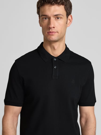 Männermodel trägt Poloshirt aus Baumwolle von MARC O’POLO DENIM in Schwarz, klassische Knopfleiste, Logo, Nahaufnahme Oberkörper.