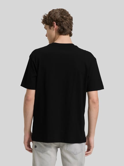 Mannenmodel draagt Relaxed Fit T-Shirt aus reiner Baumwolle van Tom Tailor Denim, effen zwart, labelprint, ronde hals, korte mouw, puur katoen, volledige lichaamsweergave achteraan.