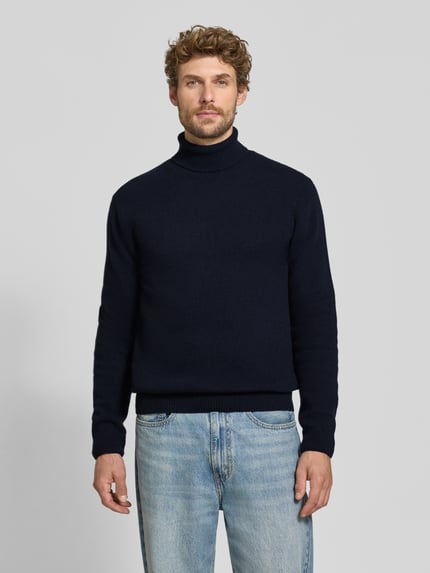 Męski model nosi Slim Fit Rollkragenpullover aus Woll-Mix Modell 'Karl' von Casual Friday, kolor granatowy, prążkowane wykończenia, mieszanka wełny, długi rękaw, prążkowany kołnierz, długość tyłu w rozmiarze M: 70 cm, długość rękawów w rozmiarze M: 69 cm. Ganzkörperansicht von vorne.