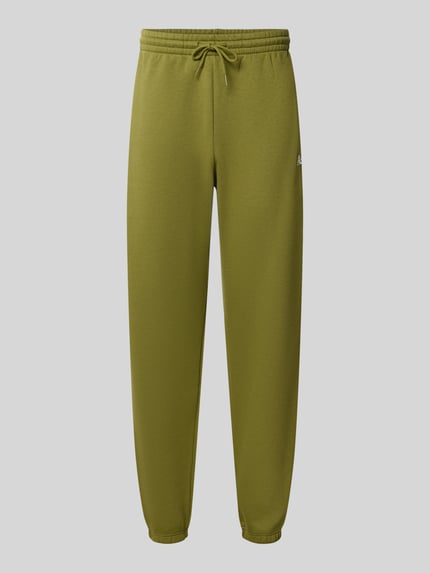 Produktfoto, Regular Fit Sweatpants aus Baumwoll-Mix mit Label-Stitching von New Balance in Olivgrün, elastischer Bund und Tunnelzug, glatte Oberfläche, Herren Sweatpants, Innenbeinlänge 79 cm, schlichte Form.