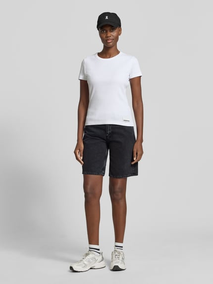 Frauenmodel trägt Regular Fit Jeansshorts aus reiner Baumwolle Modell 'THALINAA' von Armedangels in schwarzer Denim-Optik, mit Label-Patch, Gürtelschlaufen, Knopf und verstecktem Reißverschluss, 5-Pocket-Design, Materialverarbeitung Twill, Ganzkörperansicht von vorne.