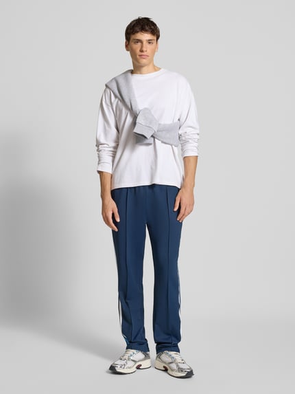 Männermodel trägt Trackpants mit elastischem Bund Modell 'LATUCCI' von Ellesse in Dunkelblau mit weißen Galonstreifen, lockerer Passform, Ganzkörperansicht von vorne.