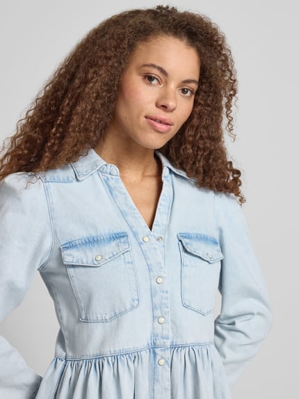 Frauenmodel trägt Mini-Jeanskleid aus reiner Baumwolle Modell 'CYRUS' von Only in heller Denim-Optik mit V-Ausschnitt, Nahaufnahme Oberkörper.