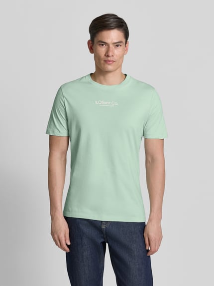 Mężczyzna model nosi Regular Fit T-Shirt aus reiner Baumwolle von s.Oliver RED LABEL, jasna zieleń, prosty krój, jednolity kolor, krótki rękaw, okrągły dekolt, bawełniany dżersej, nadruk z logo, Ganzkörperansicht von vorne.