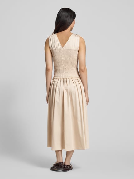 Frauenmodel trägt Midikleid mit Smok-Detail von Comma, cremefarben, Baumwoll-Mix, Taillierte Passform, Ärmelloses-Design, Ganzkörperansicht Rückansicht.