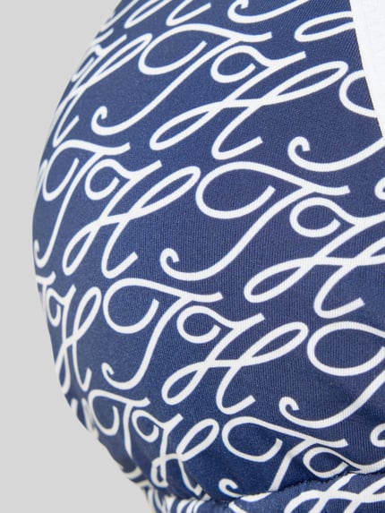 Frauenmodel trägt Neckholder Bikini-Oberteil mit Label-Print von TOMMY HILFIGER in Blau mit weißem Allover-Muster, Detailaufnahme.