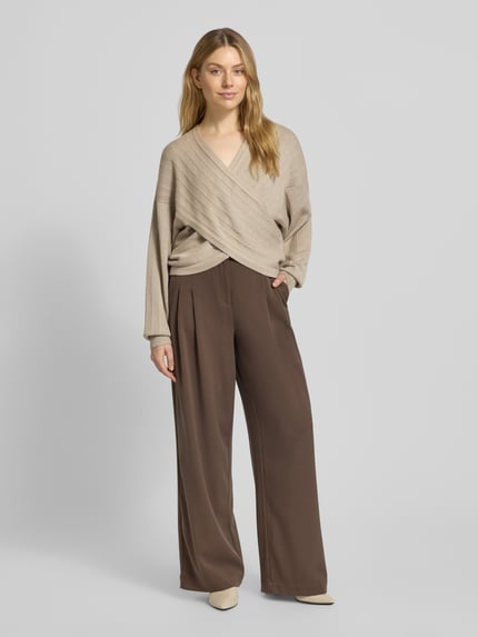 Vrouwenmodel draagt Strickpullover in Wickel-Optik Modell 'Zine Rachelle' van MSCH Copenhagen in beige, V-hals, relaxed fit, vooraanzicht volledig lichaam.