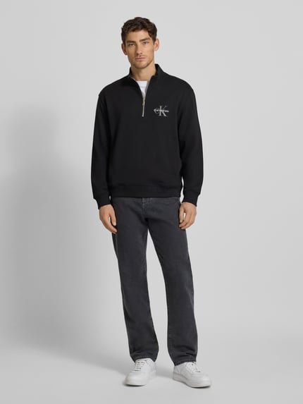 Männermodel trägt Regular Fit Sweatshirt mit Logo-Stitching Modell 'Terry' von Calvin Klein Jeans in Schwarz, Ganzkörperansicht von vorne. Elastischer Baumwoll-Mix, Logo-Print, elastische Abschlüsse, Troyer-Kragen.