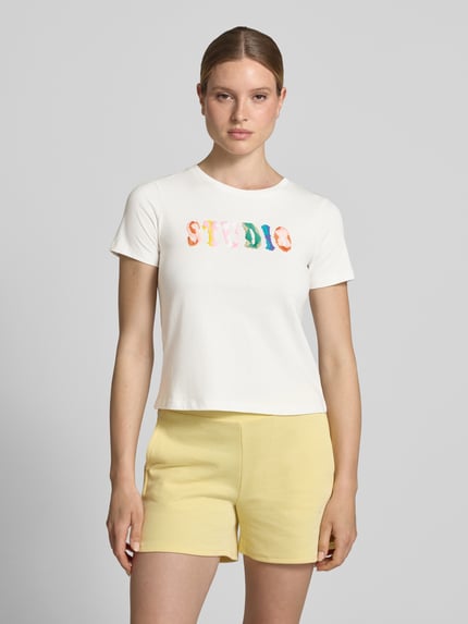 Modelka nosi Regular Fit T-Shirt mit Logo-Stitching od JAKE*S STUDIO WOMAN z czystej bawełny, biały, okrągły dekolt, długość tyłu 51 cm w rozmiarze S, krótki rękaw, kolorowy haft na klatce piersiowej, krój regular fit, widok całej sylwetki z przodu.